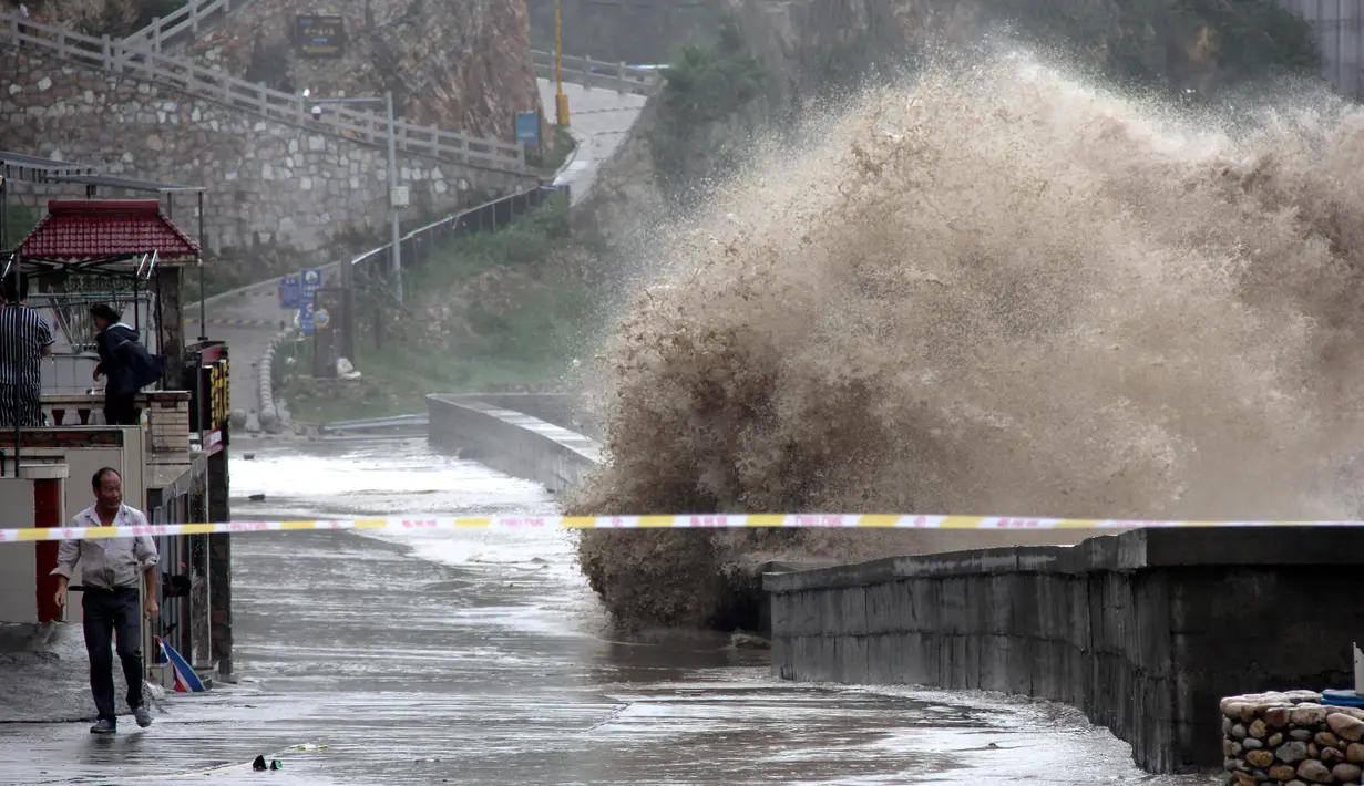 Seorang pria berjalan di dekat ombak besar yang menghantam tembok di pantai dekat Wenling, Provinsi Zhejiang, China, Rabu (11/7). Terpaan Topan Maria menyebabkan ombak besar terjadi di wilayah tersebut. (AFP)