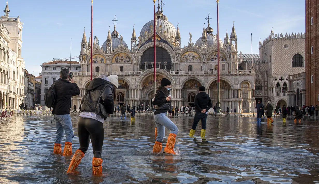 Orang menggunakan jembatan trestle untuk menyeberangi St Mark's Square yang dibanjiri air laut, di Venesia, Italia, Sabtu (4/12/2021). Air mencapai 99 sentimeter di atas permukaan laut dan bagian terendah kota tenggelam. (AP Photo/Luigi Costantini)