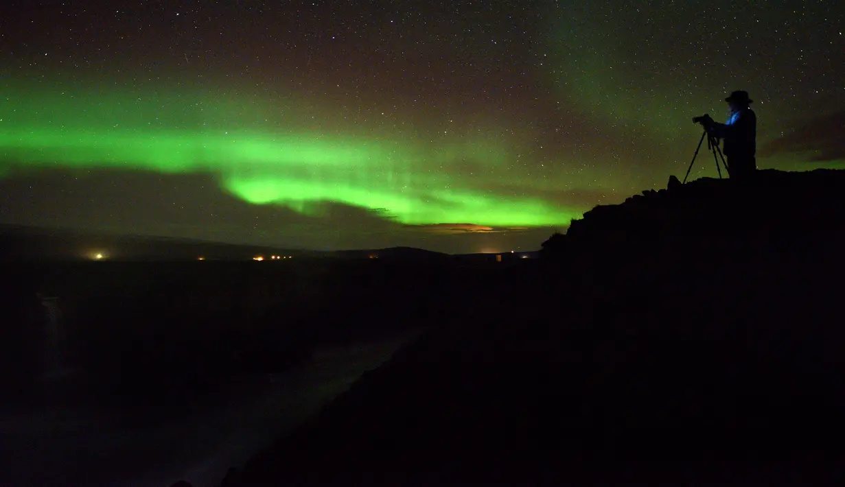 Seorang pria mengambil gambar aurora borealis atau Cahaya Utara yang terlihat di atas air terjun Godafoss di Thingeyjarsveit, Islandia, 14 Oktober 2018. Seperti halnya pelangi, Aurora Borealis memiliki gradasi warna yang beragam. (Mariana SUAREZ/AFP)