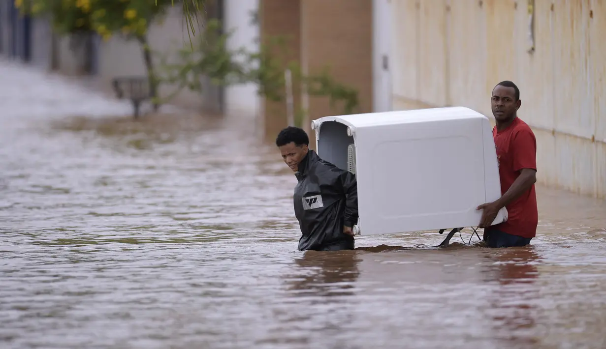 Orang-orang mengarungi air saat mereka memindahkan barang-barang dari rumah mereka yang terendam banjir di negara bagian Minas Gerais di kotamadya Juatuba, Brasil (10/1/2022). Hujan deras yang turun dalam beberapa hari terakhir di bagian tenggara negara itu membuat banjir besar. (AFP/Douglas Magno)