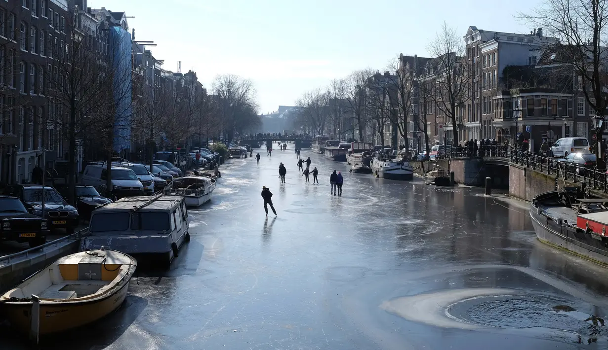 Orang-orang berseluncur dan berjalan melintasi permukaan kanal Prinsengracht yang membeku di Amsterdam, Belanda, Jumat (2/3). Banyak juga wisatawan yang melakukan swafoto untuk mengabadikan momen langka ini. (AP/Mike Corder)