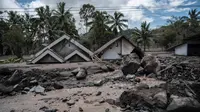 Batu-batu besar tersebar di depan rumah-rumah yang rusak di Dusun Kamar Kajang, Lumajang, Kamis (9/12/2021). Luapan air sungai bercampur material lahar dingin erupsi Gunung Semeru merendam puluhan rumah akibat diguyur hujan deras pada Selasa (7/12) dan Rabu (8/12) malam. (Juni Kriswanto/AFP)