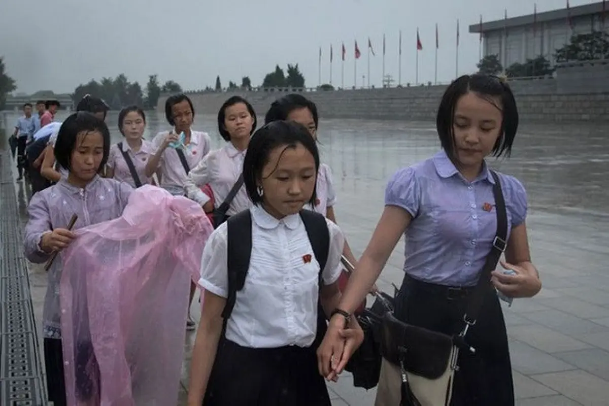 Para siswa tengah berjalan meski hujan deras untuk memberi penghormatan kepada mantan pemimpin Korea Utara Kim Il Sung dan Kim Jong-Il di luar Istana Kumsusan saat negara tersebut menandai 'Hari Kemenangan' di Pyongyang (AFP/Ed JONES)