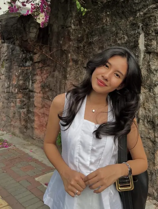 Wajahnya dipulas makeup minimalis dengan mengaplikasikan blush on coral di pipi, lipstik pink. Rambut panjang hitam terurai dengan gaya wavy dan poni belah tengah.  [@sheninacinnamon]