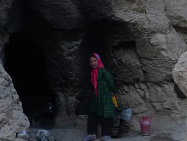 Seorang gadis kecil berdiri di pintu masuk gua di kota Bamiyan, Kabul. Foto diambil pada 19 Juni 2015. Ratusan warga miskin Afghanistan terpaksa menghuni gua-gua tersebut untuk dijadikan rumah karena tak memiliki tempat tinggal. (AFP PHOTO / SHAH Marai)