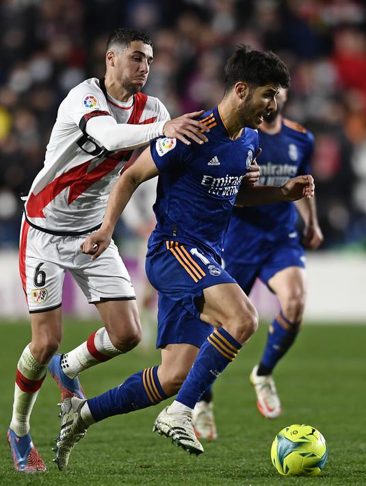 Gelandang Real Madrid, Marco Asensio membawa bola dari kawalan pemain Rayo Vallecano, Santi Comesana pada pertandingan La Liga Spanyol di stadion Vallecas di Madrid, Spanyol, Minggu (27/2/2022). Real Madrid menang tipis atas Rayo Vallecano 1-0. (AP Photo/Jose Breton)