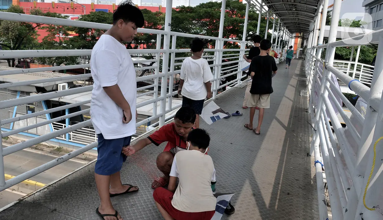 Sejumlah anak berusaha menerbangkan layangan dari Jembatan Penyeberangan Orang (JPO) di Jakarta, Kamis (11/6/2020). Minimnya ruang terbuka di sekitar tempat tinggal anak-anak itu menyebabkan mereka terpaksa bermain layang-layang di JPO yang sangat berisiko dan berbahaya. (merdeka.com/Iqbal Nugroho)