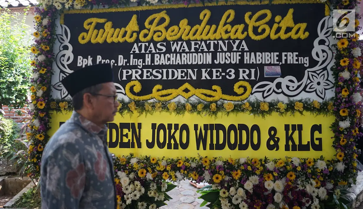 Pelayat melewati karangan bunga dari Presiden Joko Widodo yang menghiasi jalan menuju rumah duka Presiden ke-3 RI BJ Habibie di Kuningan, Jakarta, Kamis (12/9/2019). Habibie meninggal pada usia 83 tahun akibat gagal jantung dan menua. (Liputan6.com/Immanuel Antonius)