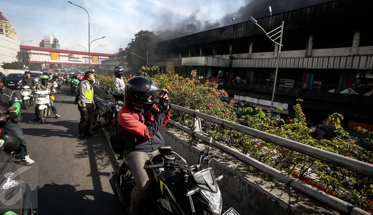 Seorang pengendara motor mengambil gambar kebakaran yang melanda Blok III Pasar Senen, Jakarta Pusat, Kamis (19/1). Banyak warga yang melintas melambatkan laju kendaraannya untuk melihat kebakaran Pasar Senen. (Liputan6.com/Faizal Fanani)