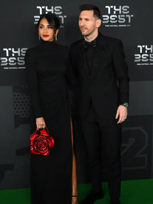 Pemain Paris Saint-Germain asal Argentina, Lionel Messi (kanan) dan istrinya Antonela Roccuzzo berpose setibanya pada acara The Best FIFA Football Awards 2022 di Paris, Prancis, 27 Februari 2023. Antonella menenteng tas merah mawar, senada dengan warna lipstik yang menghiasi bibirnya. (FRANCK FIFE/AFP)