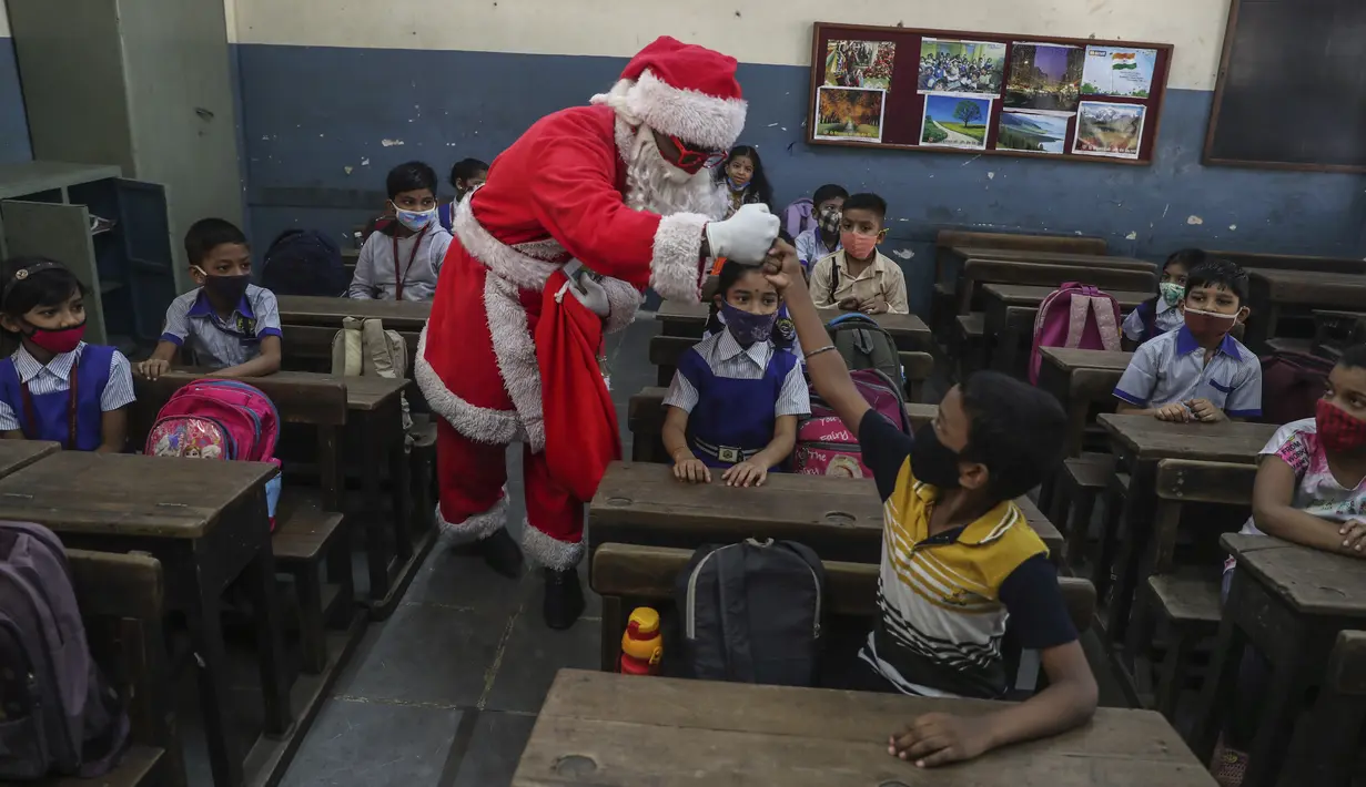 Seorang pria berpakaian Sinterklas menyapa siswa saat bersiap untuk memulai kelas tatap muka di sebuah sekolah di Mumbai, India, Rabu (15/12/2021). Setelah ditutup selama hampir 20 bulan karena pandemi virus corona, sekolah di Mumbai dibuka kembali untuk kelas 1 sampai 7. (AP Photo/Rafiq Maqbool)