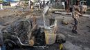 Tentara Somalia melewati puing kendaraan di lokasi ledakan bom mobil dekat pos pemeriksaan parlemen dan Kementerian Dalam Negeri di Mogadishu, Minggu (25/3). Ledakan terjadi di kawasan yang dijaga dengan sangat ketat di kota itu. (AP/Farah Abdi Warsameh)