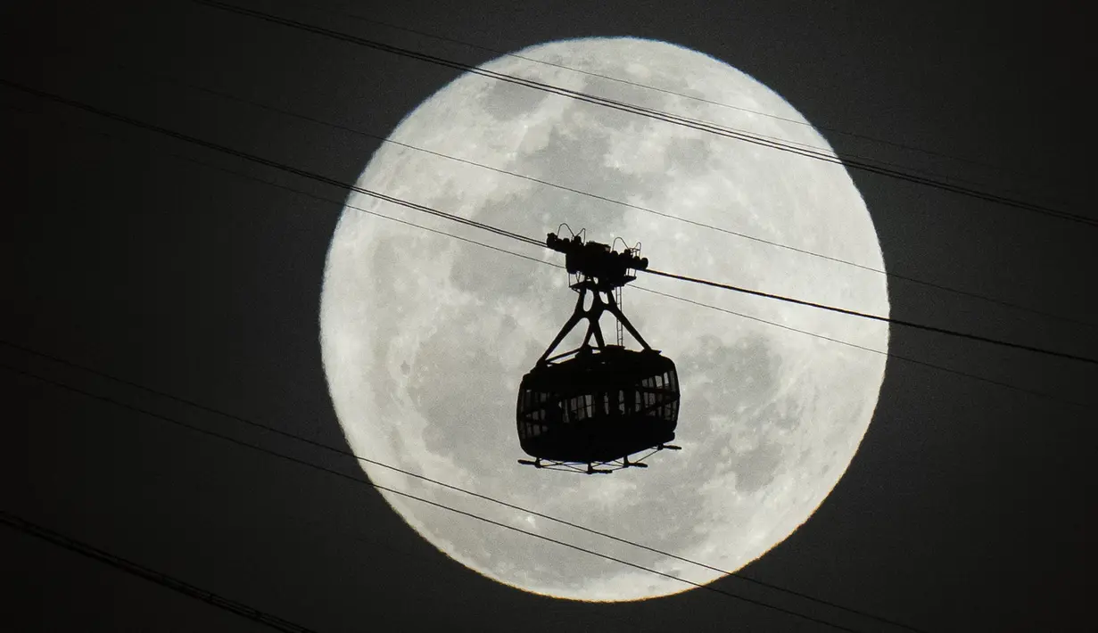 Kereta gantung bergerak menuju gunung Sugar Loaf saat supermoon terbit di langit malam di Rio de Janeiro, Brasil, Selasa, 1 Agustus 2023.  Supermoon secara umum didefinisikan sebagai bulan purnama yang berada lebih dekat ke Bumi daripada biasanya. Hal ini membuatnya tampak sedikit lebih terang dan lebih besar di langit. (AP Photo/Silvia Izquierdo)