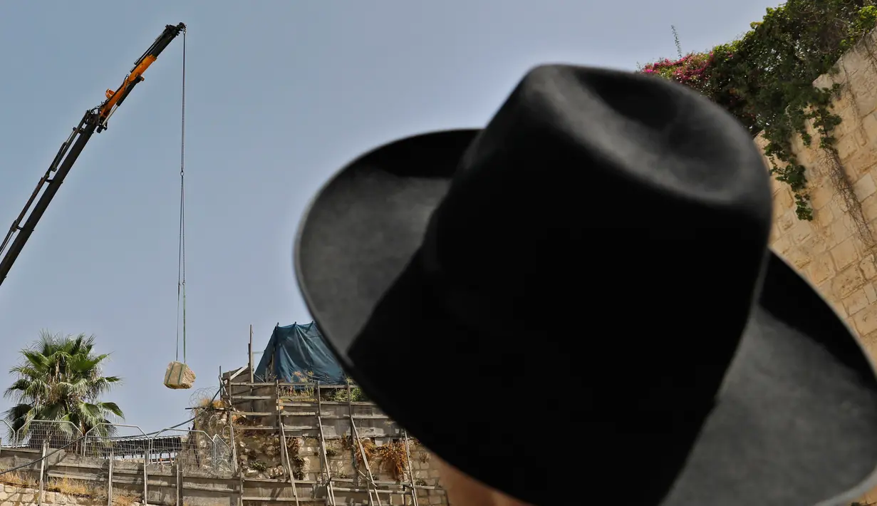 Seorang pria Yahudi Ortodoks menyaksikan para pekerja Otoritas Barang Antik Israel menggunakan crane untuk memindahkan sebuah batu besar yang jatuh dari Tembok Ratapan dua hari sebelumnya di Kota Tua Yerusalem, Rabu (25/7). (AFP/AHMAD GHARABLI)