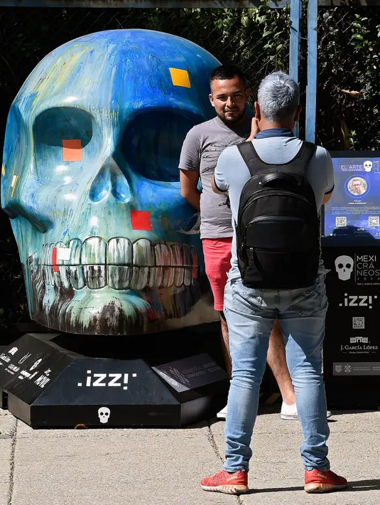 Seorang pria berpose dengan tengkorak yang dihias selama pameran edisi keempat "Mexicraneos" (Mexisculls) di Reforma Avenue, Mexico City pada 23 Oktober 2020. Instalasi sebanyak 55 tengkorak berbagai warna tersebut menghiasi jalanan sebagai bagian dari perayaan Day of the Dead (ALFREDO ESTRELLA/AFP)