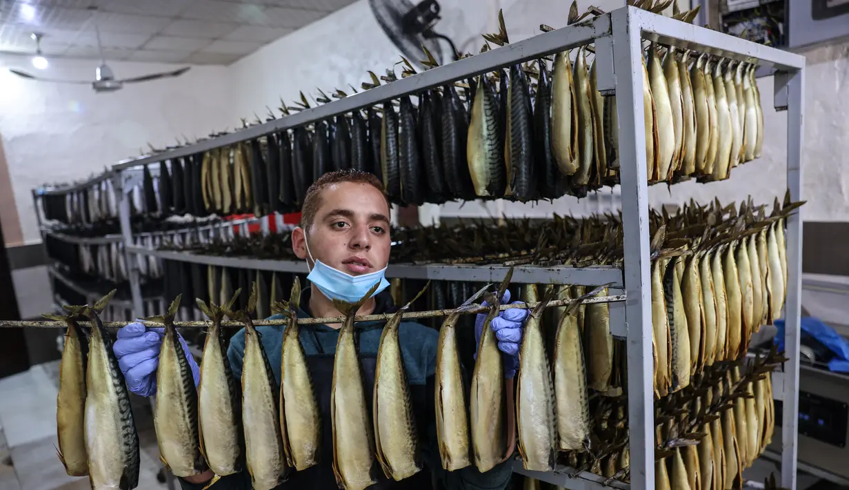 Seorang pemuda Palestina mengasapi makarel untuk dijual di pasar ikan menjelang liburan Idul Fitri di kota Rafah di Jalur Gaza selatan (3/5/2021). Ikan asap makarel menjadi salah satu menu hidangan buka puasa terfavorit bagi warga Gaza selama Ramadan. (AFP/Said Khatib)