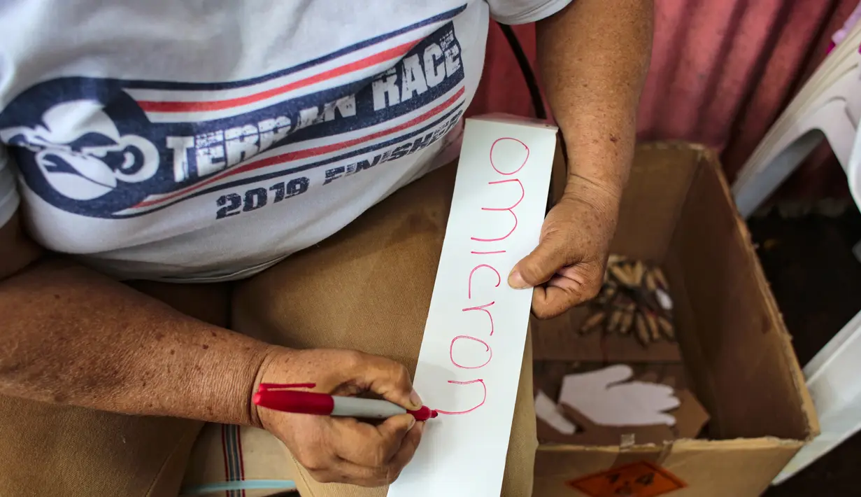 Seorang perempuan menulis kata "Omicron" di selembar kertas yang akan ditempelkan pada boneka buatan tangan di Managua, Nikaragua, Senin (27/12/2021). Boneka-boneka itu dibakar pada 31 Desember tengah malam sebagai tradisi mengucapkan selamat tinggal pada tahun yang lama. (OSWALDO RIVAS/AFP)