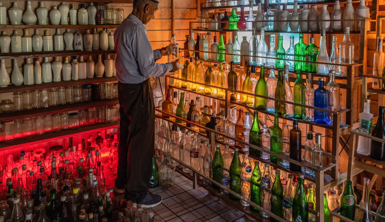 Tengku Mohamad Ali Mansor memeriksa botol kaca di museum botolnya di desa Penarik di Malaysia pada 12 September 2020.  Upaya seorang lansia Malaysia untuk membersihkan pantai-pantai negara itu dari kaca-kaca yang terkelupas membuatnya mengumpulkan koleksi ribuan botol. (AFP/Mohd Rasfan)