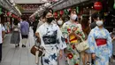 Wanita mengenakan yukata dan masker untuk melindungi diri dari penyebaran virus corona berjalan di jalan perbelanjaan Asakusa Nakamise di Tokyo, Jumat (13/8/2021). Yukata dipakai agar badan menjadi sejuk di sore hari atau sesudah mandi malam berendam dengan air panas. (AP Photo/Koji Sasahara)