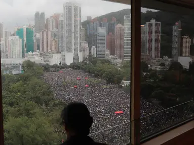 Seseorang berdiri dekat jendela melihat unjuk rasa di Victoria Park, Hong Kong, Minggu (18/8/2019). Puluhan ribu massa pro-demokrasi membawa payung saat hujan mengguyur Victoria Park dan sekitarnya. (AP Photo/Kin Cheung)