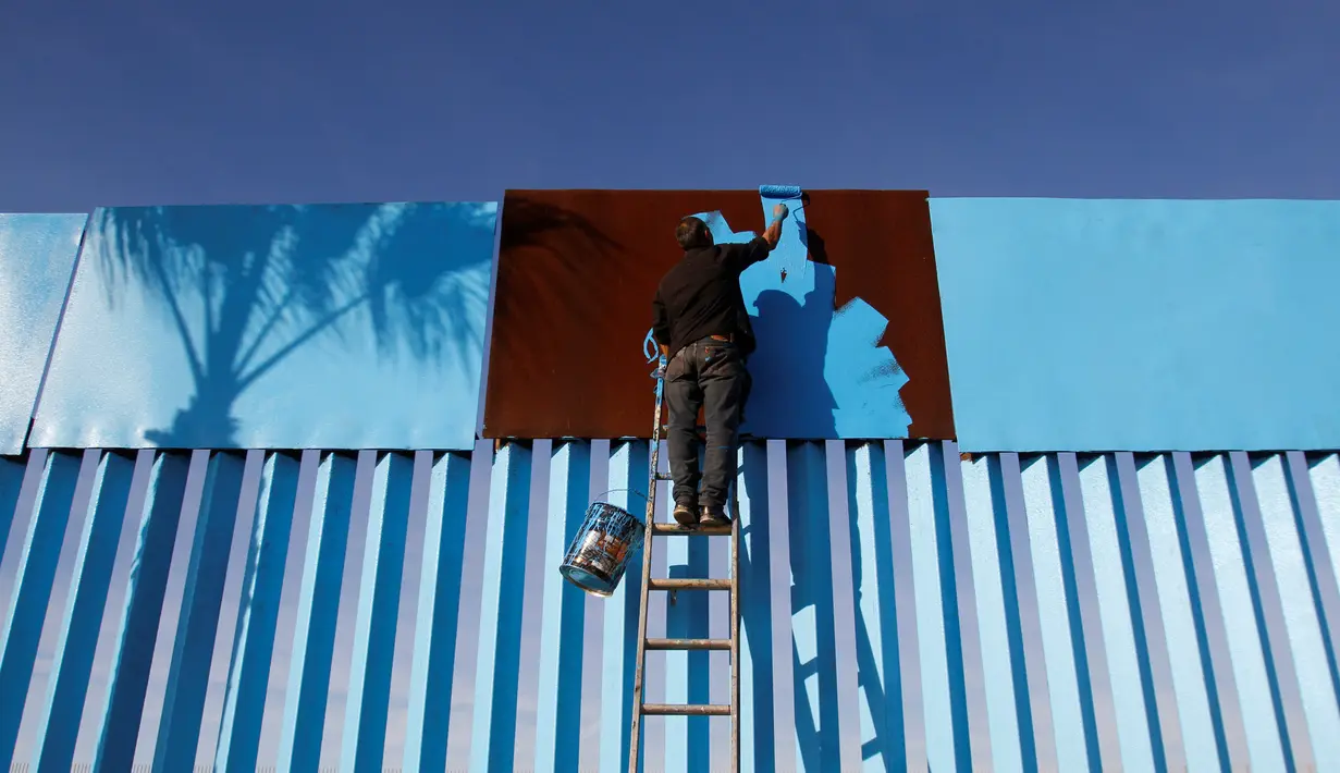 Seorang seniman menyelesaikan pengecatan pagar yang memisahkan antara Meksiko dan Amerika Serikat di Playas Tijuana, Meksiko (10/12). (Reuters/Jorge Duenes)