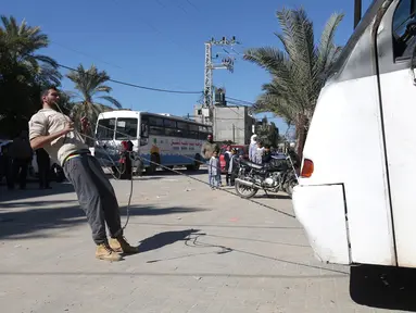 Mohamed Barka, pria yang dijuluki "Super Hero" asal Palestina menarik sebuah bus dengan gigi dalam aksinya di Deir Al-Balah, Gaza Tengah, Kamis (4/2). (MOHAMMED ABED/AFP)