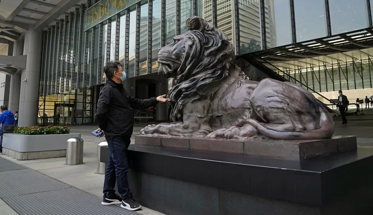Seorang pria yang mengenakan masker menyentuh patung singa perunggu di kantor pusat HSBC di Hong Kong, Jumat (4/3/2022). Pemimpin Hong Kong awal pekan ini mengatakan mobilitas orang mungkin dibatasi selama tes covid-19 massal wajib ketika kasus harian mencapai rekor. (AP Photo/Kin Cheung)