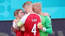 Kapten Denmark, Simon Kjaer dan Kasper Schmeichel, berusaha menenangkan istri Christian Eriksen, Sabrina Kvist Jensen, usai kolaps saat melawan Finlandia pada laga Piala Eropa di Stadion Parken (12/6/2021). (AFP/Wlofgang Ratttay)