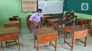 Petugas merapikan meja dan kursi jelang dibukanya pembelajaran tatap muka di SMK PB Soedirman 2, Jakarta, Selasa (6/4/2021). Uji coba pembelajaran tatap muka akan dilakukan di 5 madrasah, 1 PKBM, 42 SD, 13 SMP, 9 SMA, dan 30 SMK. (Liputan6.com/Herman Zakharia)
