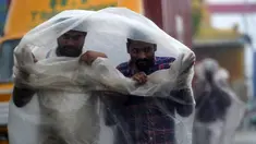 Dua pria menggunakan lembaran plastik untuk menutupi hujan lebat di Chennai saat topan Nivar mendekati pantai tenggara negara itu (25/11/2020). (AFP/Arun Sankar)