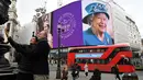 <p>Pasangan berfoto saat bus London merah lewat, di mana gambar Ratu Elizabeth II ditampilkan pada layar digital besar untuk menandai dimulainya Platinum Jubilee di Piccadilly Circus, 6 Februari 2022. Ratu Elizabeth II menjadi raja Inggris pertama yang memerintah selama tujuh dekade. (Daniel LEAL/AFP)</p>