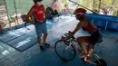 Atlet triathlon Kuba, Leslie Amat mengendarai sepedanya, diadaptasi menjadi stasioner, di bawah pengawasan pelatihnya Dioseles Fernandez di teras rumahnya di Havana, Senin (20/4/2020). Atlet Kuba tak bisa berlatih di fasilitas olahraga seperti biasanya selama pademi corona. (AP /Ismael Francisco)