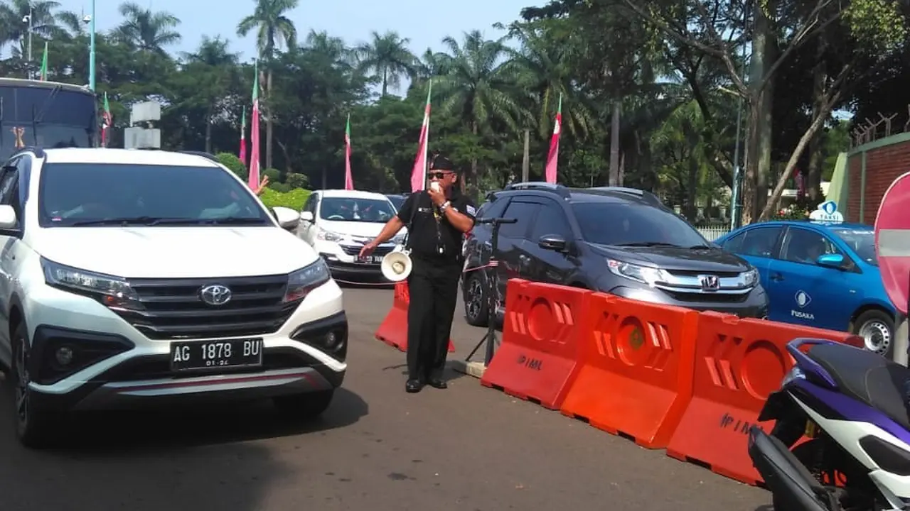 Seorang Petugas Tengah Mengatur Antrean Kendaraan di Gerbang Taman Mini Indonesia Indah (TMII), Jakarta, Sabtu (8/6/2019). (Foto: Muhammad Radityo Priyasmoro/Liputan6.com)