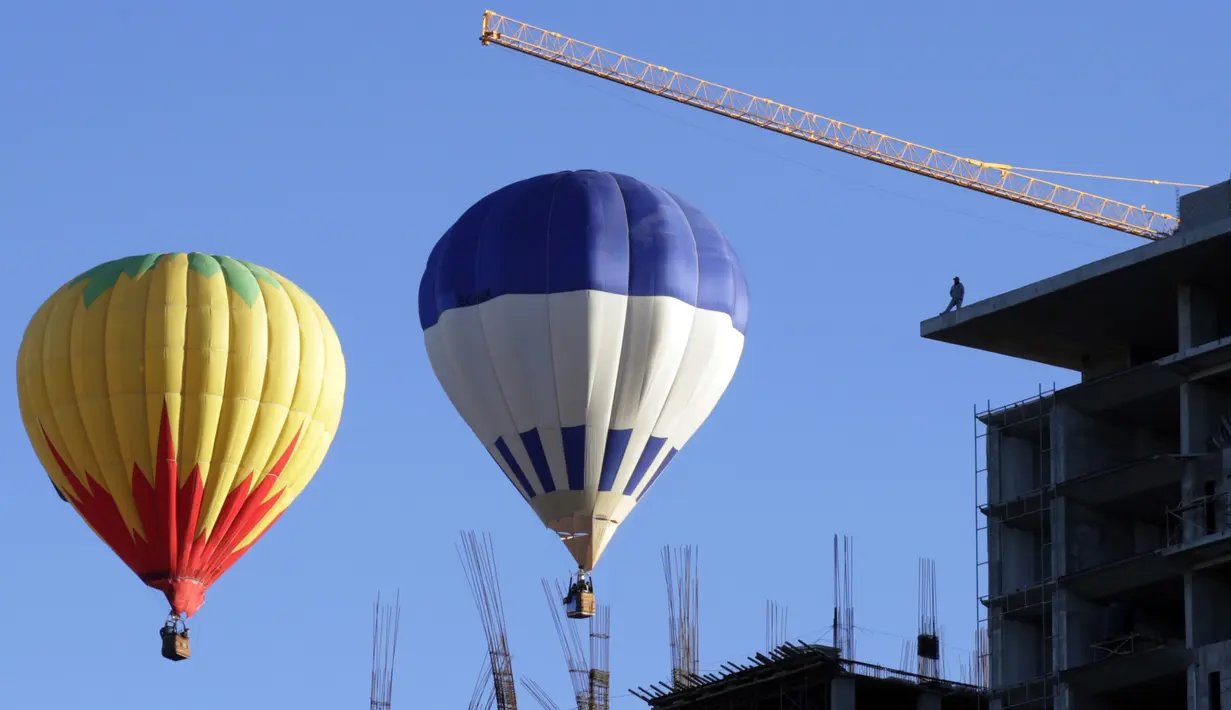 Pekerja bangunan gedung memperhatikan balon udara yang melitasinya Festival Balon Internasional ke-XV di Metropolitan Park di Leon, negara bagian Guanajuato, Meksiko (20/11). (AFP/STR)