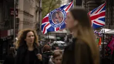 Pejalan kaki berjalan melewati kios yang menjual bendera yang mengumumkan penobatan Raja Charles di London, Jumat, 5 Mei 2023. Penobatan Raja Charles III akan berlangsung di Westminster Abbey pada 6 Mei. (AP Photo/Emilio Morenatti)