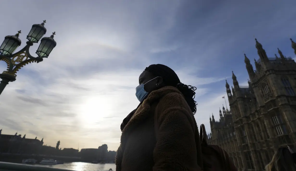 Seorang perempuan yang mengenakan masker melintasi Jembatan Westminster di London, Kamis (9/12/2021). Perdana Menteri Inggris Boris Johnson telah mengumumkan pembatasan yang lebih ketat untuk membendung penyebaran varian baru Covid-19, omicron. (AP Photo/Frank Augstein)