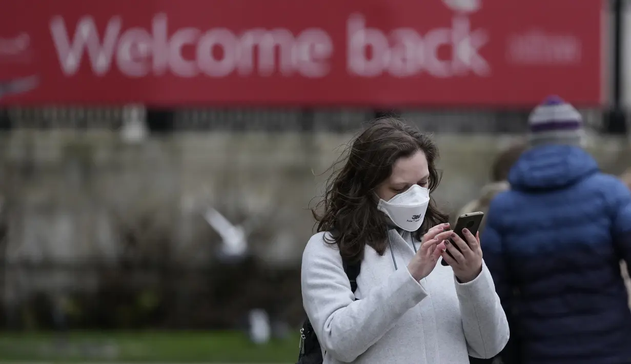 Seorang wanita mengenakan topeng untuk melindungi diri dari virus corona melihat ponselnya di Trafalgar Square, di London, Selasa (28/12/2021). Javid menuturkan, varian Omicron saat ini menyumbang sekitar 90 persen kasus baru di seluruh Inggris. (AP Photo/Alastair Grant)