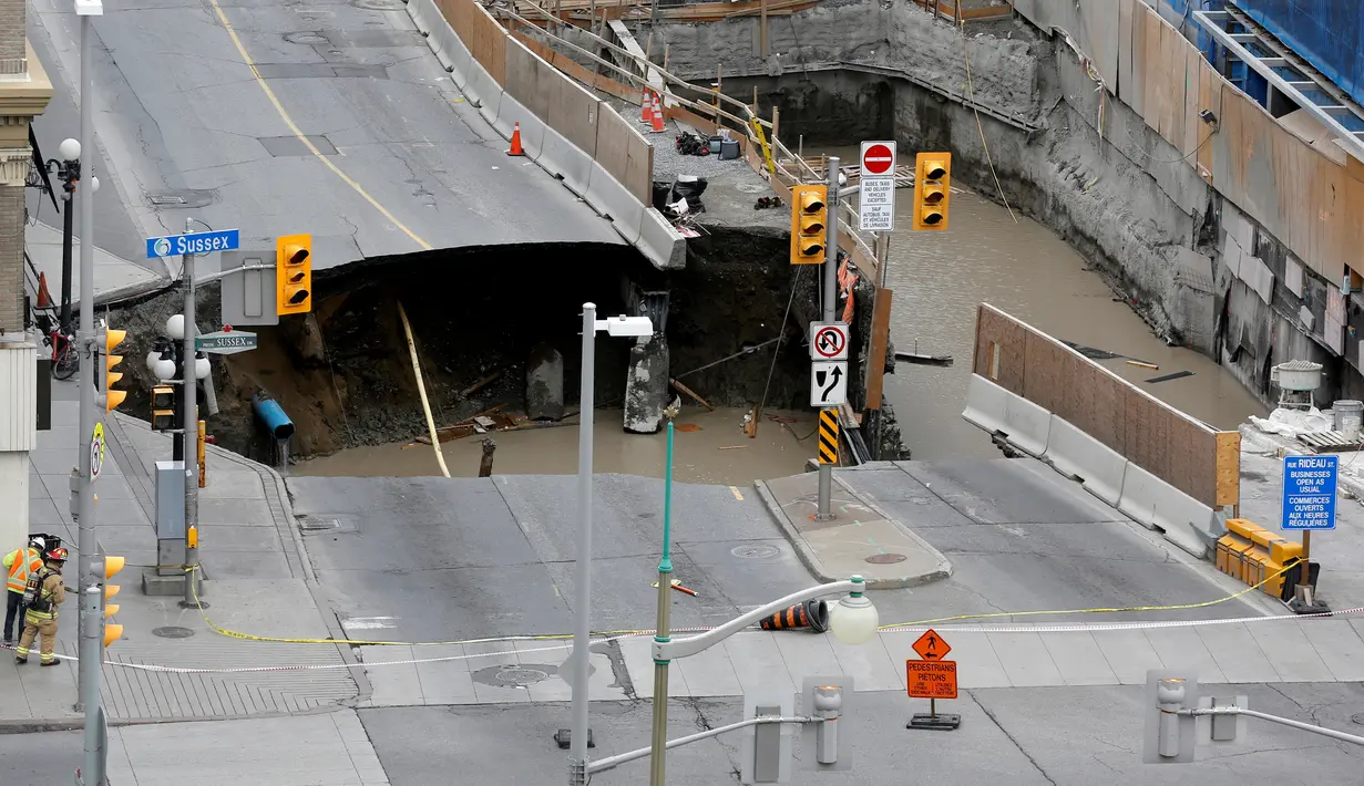 Pekerja mengamati sebuah sinkhole besar yang menganga di Rideau Street, Ottawa, Kanada, Rabu (8/6). Area tersebut berlokasi di daerah yang sedang dilakukan penggalian dan telah ditutup untuk lalu lintas semua kendaraan bermotor. (REUTERS/Chris Wattie)