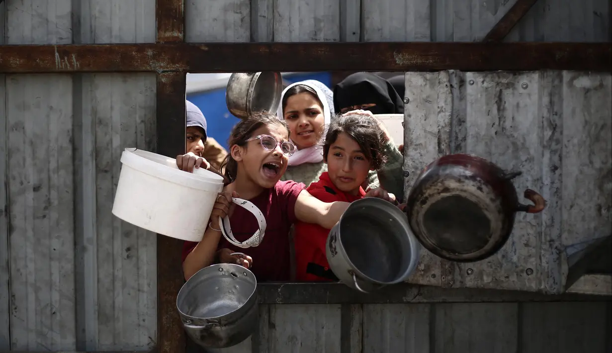 Anak-anak Palestina memberi isyarat saat mereka mengantre untuk mengambil makanan di titik distribusi makanan gratis di kamp pengungsi Nuseirat, Jalur Gaza tengah, pada 3 April 2025. (Eyad BABA/AFP)