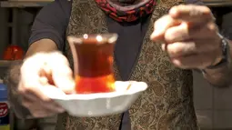 Pemilik Kazem Mabhutian menunjukkan teh buatannya di kedai teh terkecil dan tertua di gang Grand Bazaar di ibukota Iran, Teheran (20/9/2021).  Di sela-sela menuangkan segelas teh untuk pelanggannya, Kazem memberi tahu kisah seabad tentang Rumah Teh Haj Ali Darvish dengan bangga. (AFP/Atta Kenare)