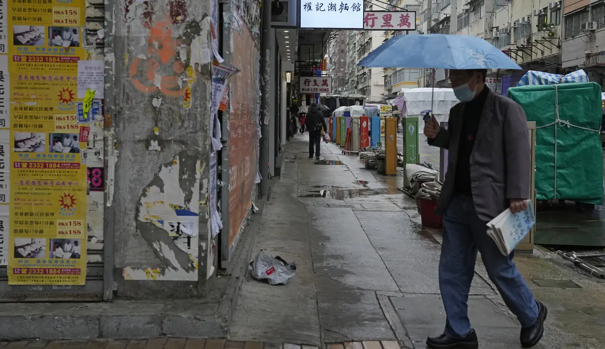 Seorang pria yang mengenakan masker, melintasi jalan di Hong Kong, pada 22 Februari 2022. Hong Kong akan melakukan pengujian Covid-19 untuk seluruh penduduknya pada bulan Maret mendatang, saat kota itu bergulat dengan wabah terburuk dari varian omicron. (AP Photo/Kin Cheung)