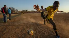 Seorang pemain berusaha mengontrol bola saat bertanding pada laga persahabatan di lapangan yang berdebu di Soweto, Afrika Selatan, Rabu (16/6/2021).  Sejumlah warga bermain bola di lapangan berdebu di Soweto, Afrika Selatan. (AP Photo/Themba Hadebe)