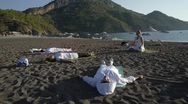 Orang-orang berlatih yoga di pantai di Adrasan, barat Antalya, Turki (24/9/2021). Orang-orang menikmati cuaca hangat di wilayah Mediterania saat salju pertama menyelimuti pegunungan tinggi di timur laut Turki. (AP Photo/Burhan Ozbilici)