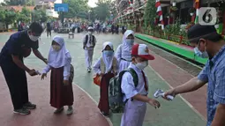 Petugas mengecek suhu badan para siswa setibanya di SDN 05 Kalisari, Jakarta, Senin (30/8/2021). Pemprov DKI menggelar pembelajaran tatap muka di tengah pandemi covid-19 mulai 30 Agustus 2021 secara terbatas dengan kapasitas 50 persen pada setiap satuan pendidikan. (Liputan6.com/Herman Zakharia)