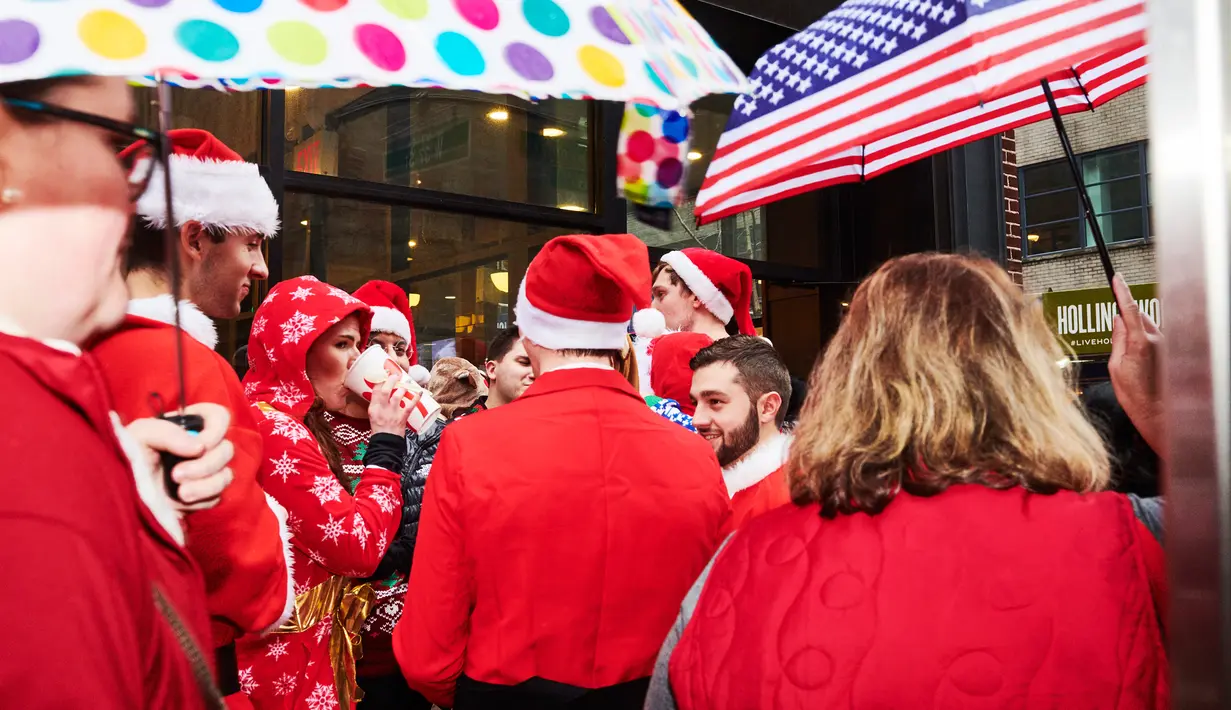 Orang-orang yang berpakaian seperti Sinterklas berdiri di tengah hujan saat berpartisipasi  dalam acara tahunan Santacon di New York City, Sabtu (14/12/2019). Dalam acara tersebut, peserta berkeliling bar untuk menyambut datangnya liburan Natal. (Gabby Jones/Getty Images/AFP)