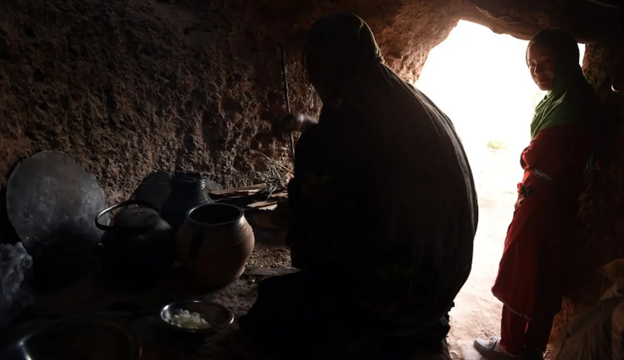 Seorang wanita bersama putrinya memasak di dalam gua di kota Bamiyan, Kabul. Foto diambil 19 Juni 2015. Ratusan warga miskin Afghanistan terpaksa menghuni gua-gua tersebut untuk dijadikan rumah karena tak memiliki tempat tinggal. (AFP PHOTO/SHAH Marai)