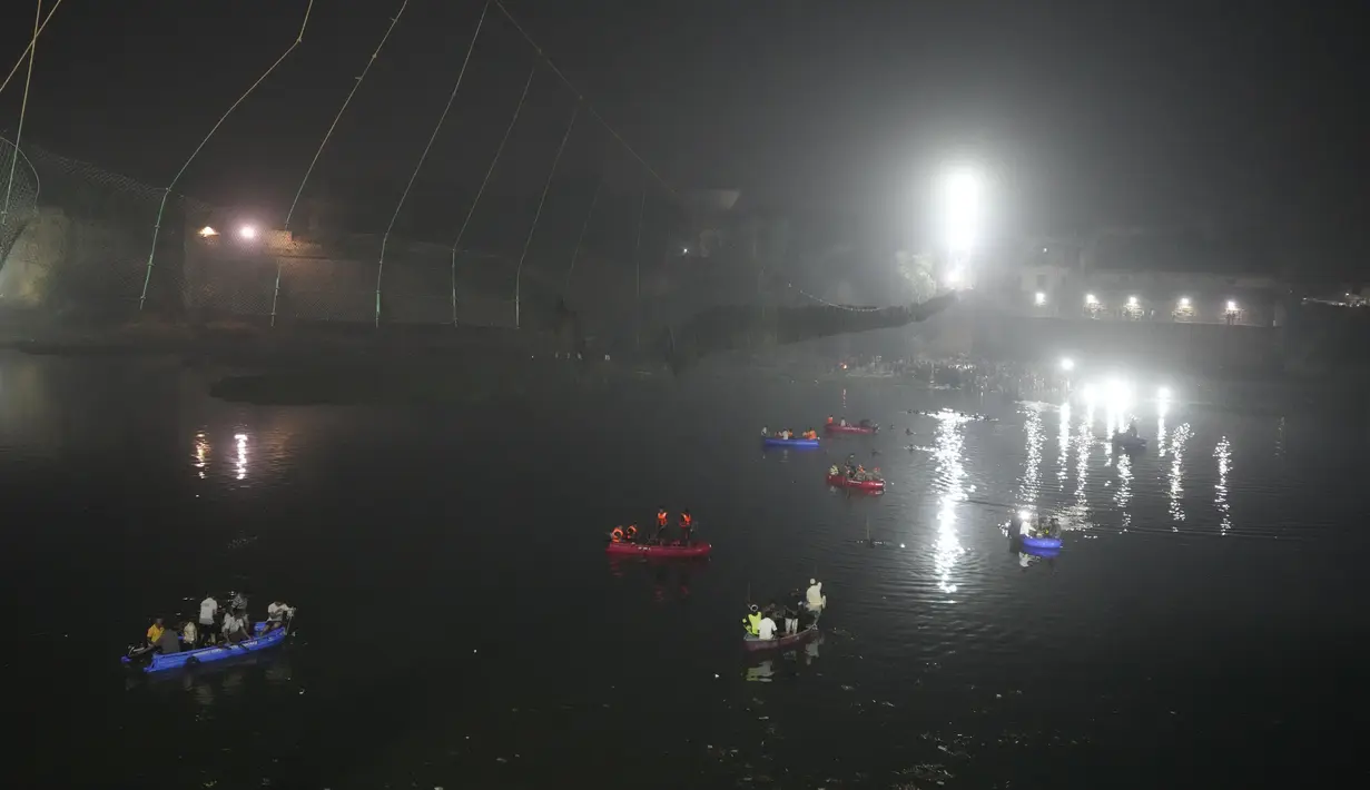 Tim penyelamat di kapal mencari di sungai Machchu di sebelah jembatan kabel yang runtuh di kota Morbi di negara bagian barat Gujarat, India, Senin, 31 Oktober 2022. Jembatan gantung kabel berusia seabad runtuh ke sungai Minggu malam, menyebabkan ratusan orang terjun. di dalam air, kata para pejabat. (AP/Ajit Solanki)