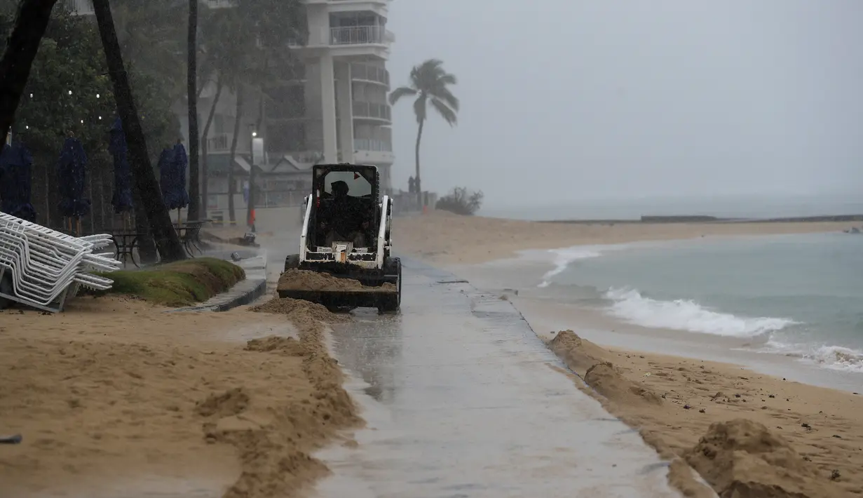 Traktor kecil mendorong pasir dari jalan setapak di Pantai Waikiki, Honolulu  (6/12/2021). Pihak berwenang mengatakan kondisi yang berpotensi lebih buruk ke depannya. (AP Photo/Caleb Jones)
