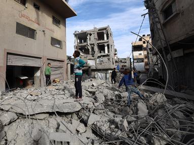Anak-anak Palestina berjalan di tengah reruntuhan bangunan yang hancur akibat serangan Israel di kamp pengungsi Bureij di Jalur Gaza bagian tengah pada 27 April 2025. (Eyad BABA/AFP)