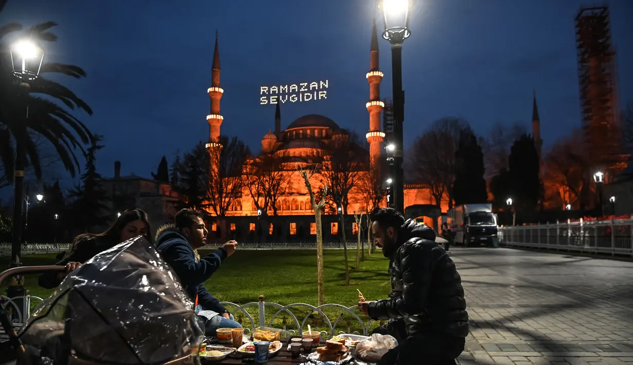 Umat Muslim berbagi Iftar, makan malam buka puasa pada hari pertama bulan puasa Ramadhan di Sultanahmet Square dengan latar belakang Masjid Biru, di Istanbul (13/4/2021). (AFP Photo/Ozan Kose)